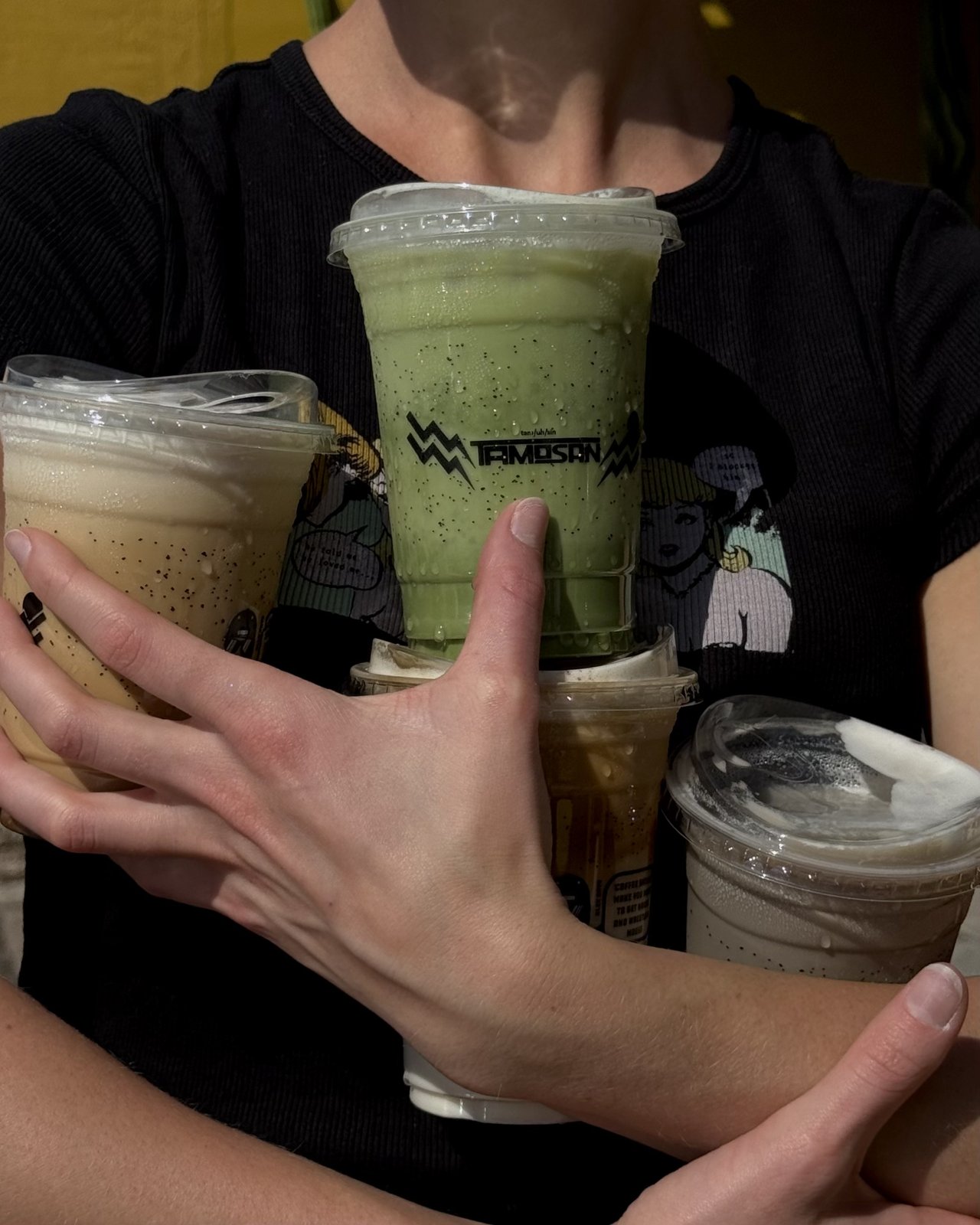 An armful of iced Tamosan drinks — matcha and iced coffee — held in the Scottsdale lounge.